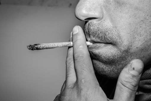 Close up portrait of a Caucasian male rolling and smoking a marijuana cigarette