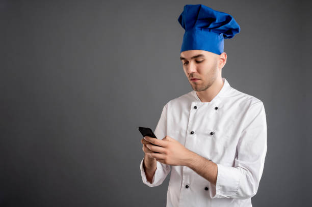 istock Young male dressed in a white chef suit reading and sending text messages on cellphone 1277769837