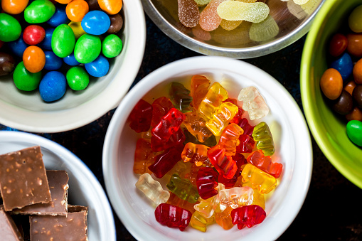 Color image depicting an overhead view of an arrangement of bowls filled with an assortment of multi-colored sweets. Room for copy space.