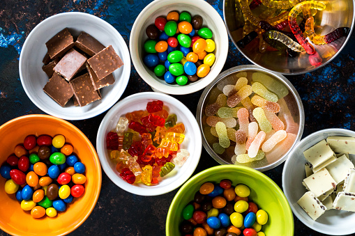 Color image depicting an overhead view of an arrangement of bowls filled with an assortment of multi-colored sweets. Room for copy space.