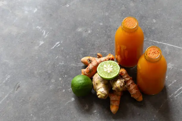 Photo of Healthy drink from turmeric and ginger roots and lime in small bottles on grey concrete background with copyspace.
