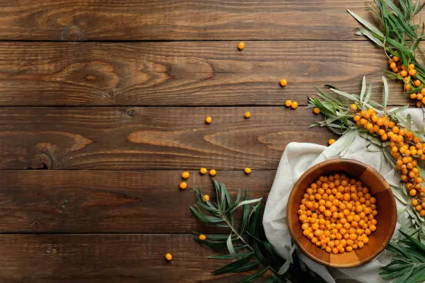 Sea buckthorn berries in bowl on wooden table. Flat lay, top view, copy space.