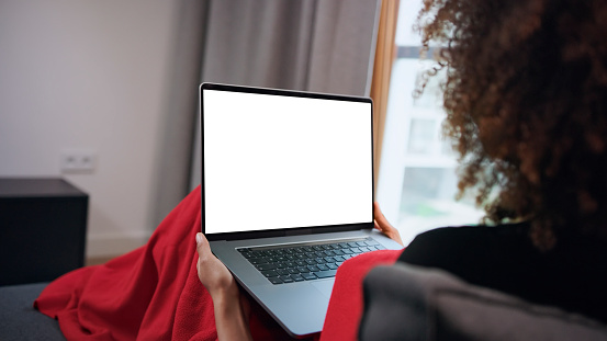 African american woman staying at home, healing on a couch. White laptop screen