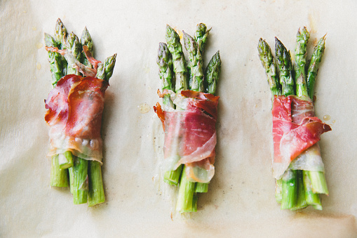 Prosciutto wrapped around 4 or 5 asparagus spears on a baking sheet
