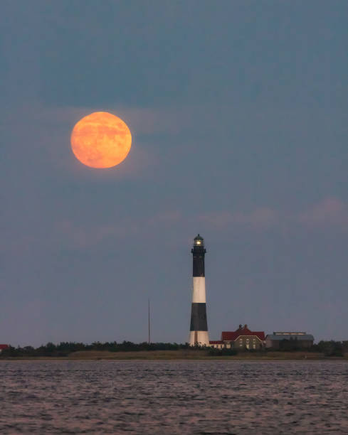istock Full moon rising through a hazy horizon behind a beautiful lighthouse.  Fire Island, NY 1277796883