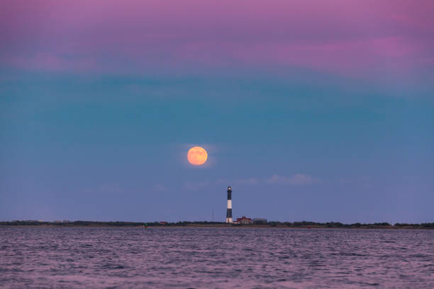 istock Full moon rising through a hazy horizon behind a beautiful lighthouse.  Fire Island, NY 1277796889