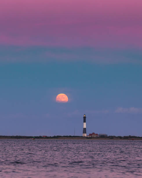 istock Full moon rising through a hazy horizon behind a beautiful lighthouse.  Fire Island, NY 1277796896