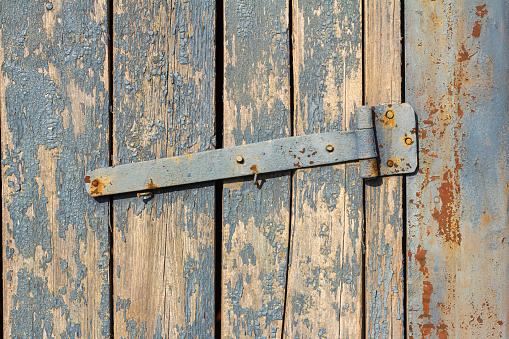 A fragment of an old wooden gate with remnants of blue paint and rusty hinges.