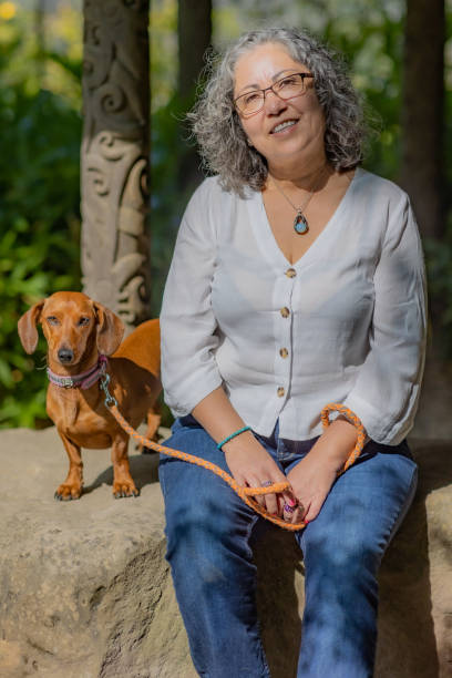 Mature Mexican woman with glasses sitting calmly together with her dachshund on a rock stock photo