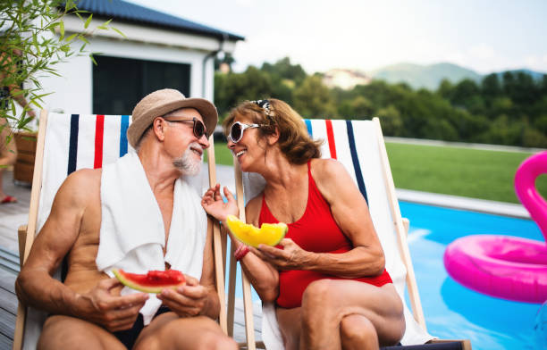 istock Cheerful senior couple sitting by swimming pool outdoors in backyard. 1277802428