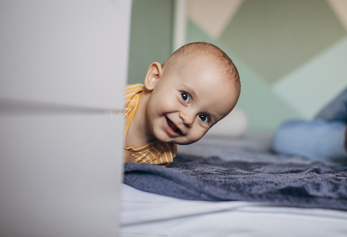 Adorable smiling baby boy lying down on the bed at home and looking at camera.