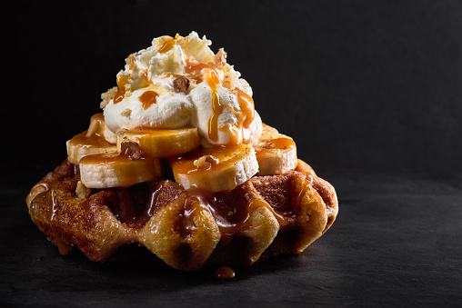 Waffles with bananas topped with caramel syrup on a dark stone background.