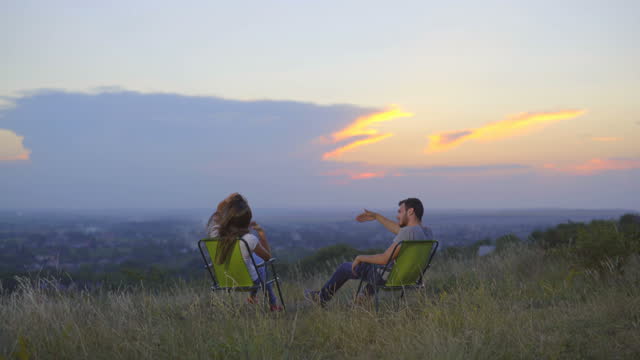 The couple sit and talk on the background of the city. Wide angle. Real time