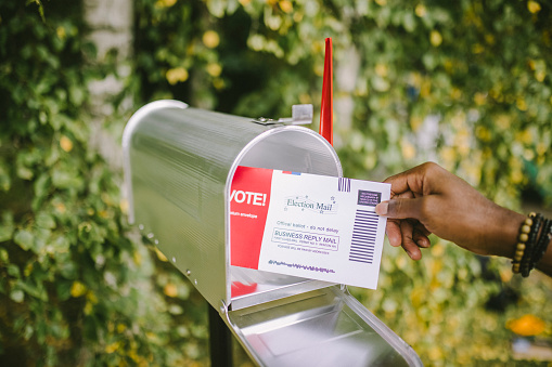 Close up of hand putting voting ballot to mailbox.