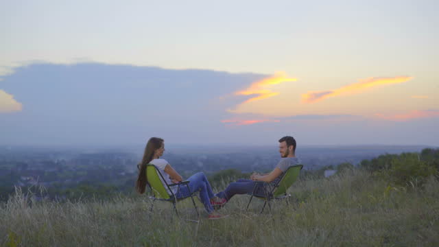 The couple sit and talk on the background of the city. Wide angle. Real time