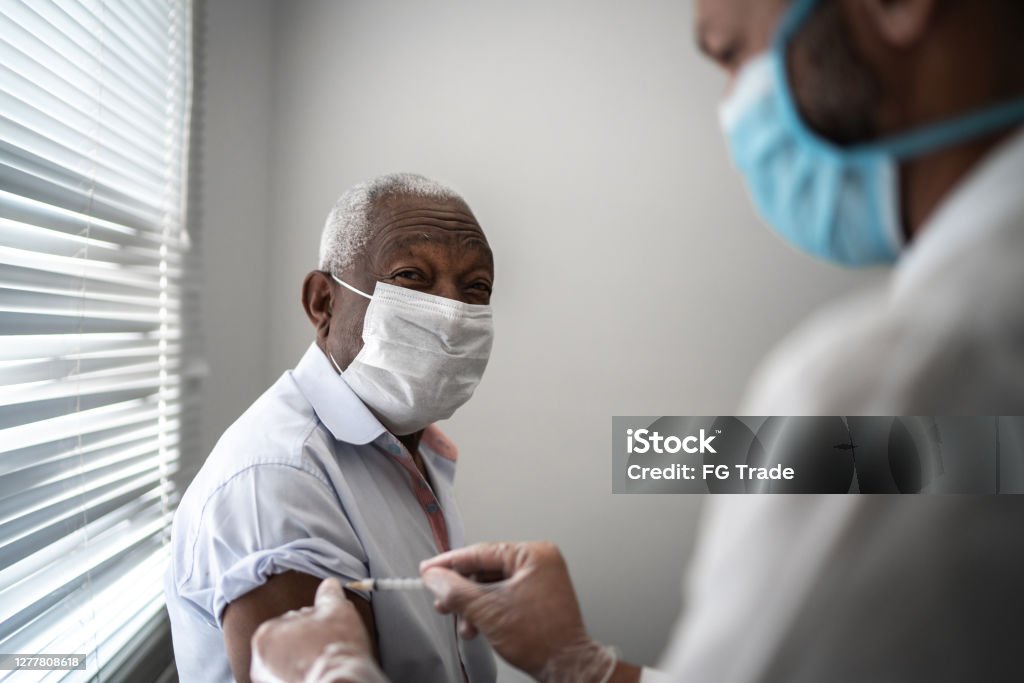 Nurse applying vaccine on patient's arm using face mask Nurse applying vaccine on patient's arm Vaccination Stock Photo