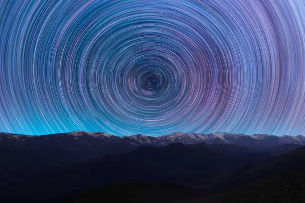 Photo of Long exposure night landscape. Beautiful mountains and. colorful star trails on the sky. Night time lapse photography.