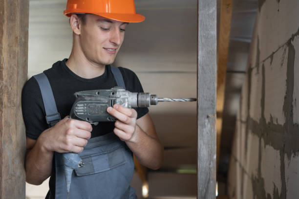 istock male builder dressed in work clothes and an orange hard hat. Holds a drill and makes a hole in a piece of wood. 1277810349