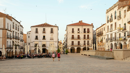 Caceres, Spain - June 23th, 2020: View of Caceres Plaza Mayor, in the historic city center, with beautiful sunset light, and tourist sitting on a terrace.