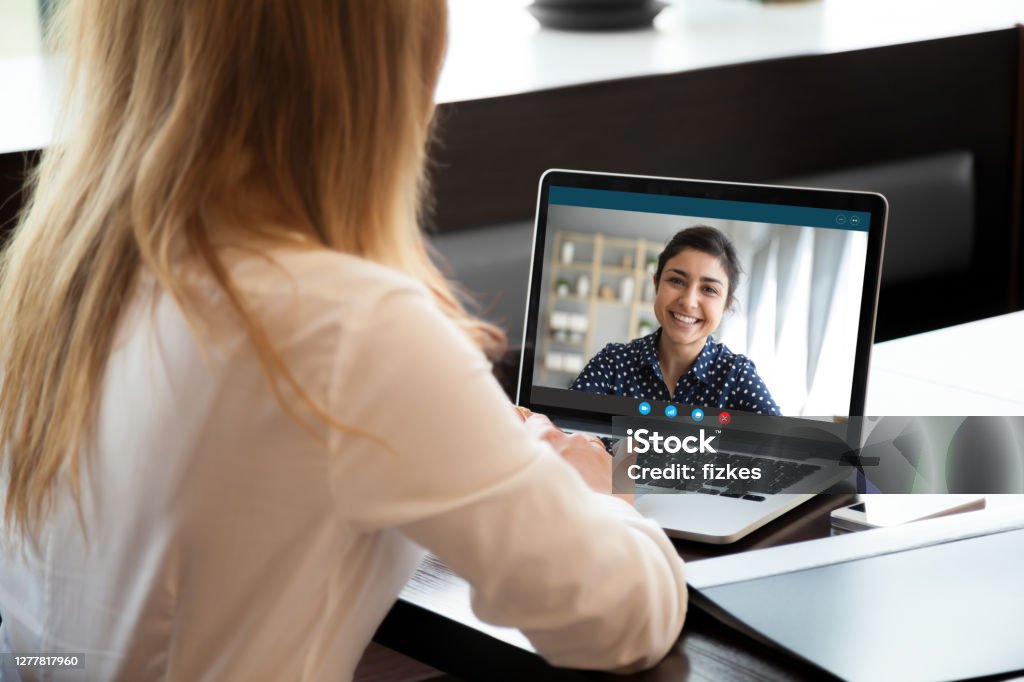 Businesswoman having distant negotiations using video conference application on pc Laptop screen view over female shoulder, businesswomen working from home on common project, company representative and client communication. Diverse girls friends chat via video conference application Internet Stock Photo