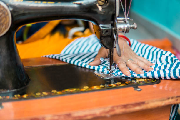 Close-up of woman hands stitching clothes by sewing machine at home.