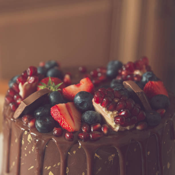 istock Appetizing chocolate cake decorated with strawberries, blueberries and a pomegranate on an orange background. 1277825611