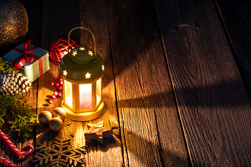 Christmas lantern candlelight beams, gifts and baubles on old rustic wooden table