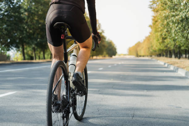 Man on a gravel bike on the road, back view. Legs of a cyclist riding a modern bicycle outdoors racing bicycle stock pictures, royalty-free photos & images