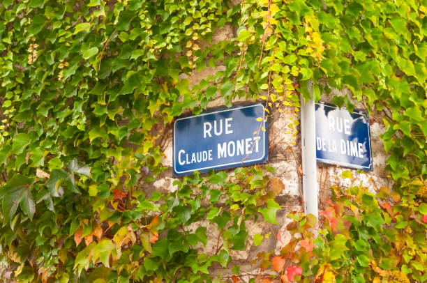 Close up of street signs on ivy covered walls at the corner of Rue Claude Monet (named after the famous impressionist painter who lived in the town) and Rue De La Dime in Giverny, France. Close up of street signs on ivy covered walls at the corner of Rue Claude Monet (named after the famous impressionist painter who lived in the town) and Rue De La Dime in Giverny, France. giverny stock pictures, royalty-free photos & images
