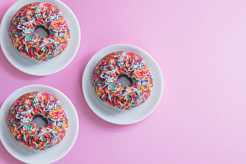 delicious donuts with multi-colored sprinkles on a pink background.