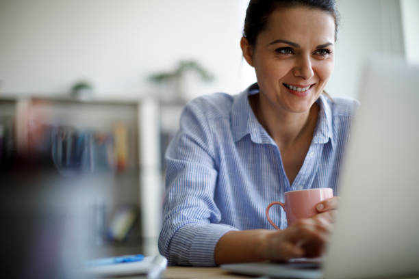 mulher madura sorridente usando laptop para trabalhar em casa - typing busy business women - fotografias e filmes do acervo
