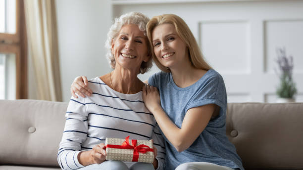 istock Grownup daughter hugging happy aged grey-haired mother holding gift box 1277840305