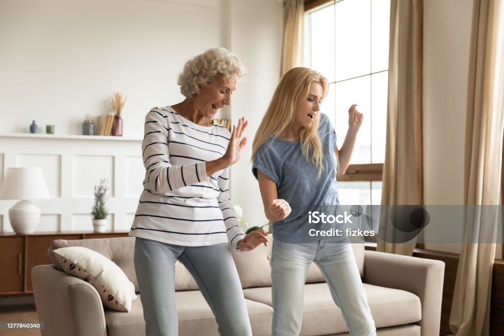 Aged granny and grown granddaughter dancing at home celebrating housewarming Improvised party. Elder and younger women best friends, aged active granny and grown grandchild girl spending time together dancing relaxing at home celebrating housewarming, purchasing new apartment Dancing Stock Photo