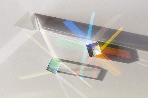 Glass geometric figures prisms with light diffraction of spectrum colors and complex reflection with trendy light and hard shadows on a white background.