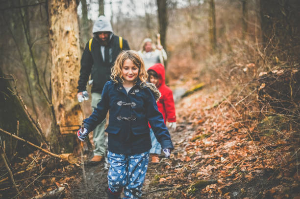 Cute kids, father and grandmother out taking a hike in late fall or winter cold. Girl reads a map