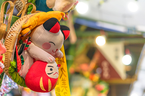 asakusa, japan - november 08 2019: Auspicious rake or engi kumade decorated with a cute plush made of japanese chirimen crêpe fabric depicting a manekineko lucky cat holding a Daruma doll in a basket.