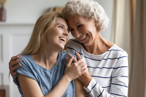Tender caring silver god-mother embracing shoulders of beloved grown god-daughter My beloved god-child. Tender caring elegant old lady god-mother embracing shoulders of grown up god-daughter, mature silver mom and adult kid girl standing close, touching foreheads and smiling pics of the godmother stock pictures, royalty-free photos & images