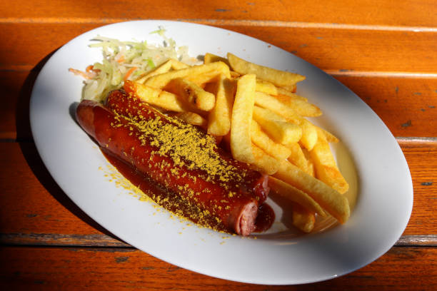 istock Traditional German currywurst, served with chips on a white plate. Wooden table as background. 1277861473