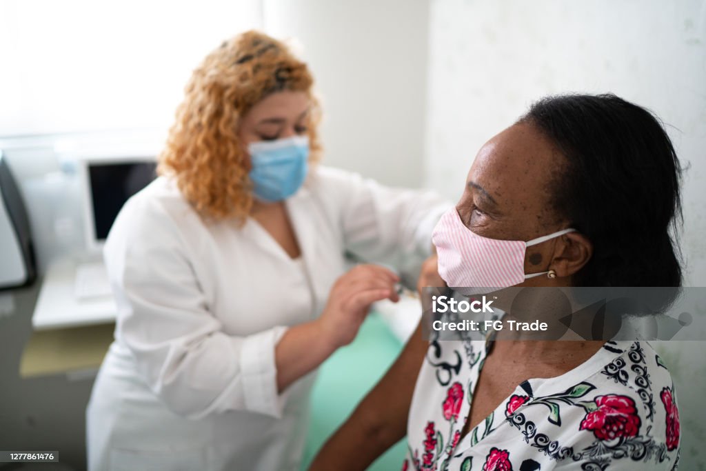 얼굴 마스크를 사용하여 환자의 팔에 백신을 적용하는 간호사 - 로열티 프리 백신접종 스톡 사진