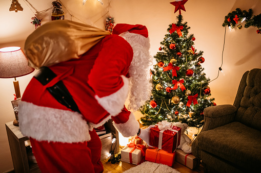 Santa Claus is secretly leaving gift under Christmas tree.