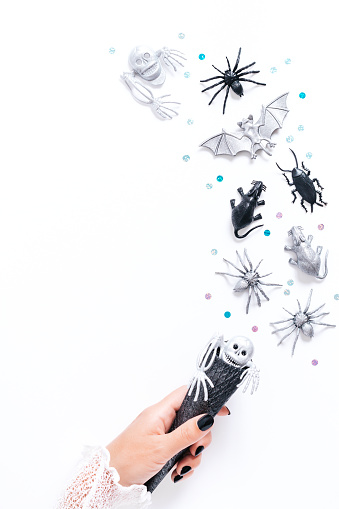 Halloween card on white background with black and silver holiday decor. Woman with black manicure holding silver cone with silver and black bats and ghosts flying around, copy space, top view