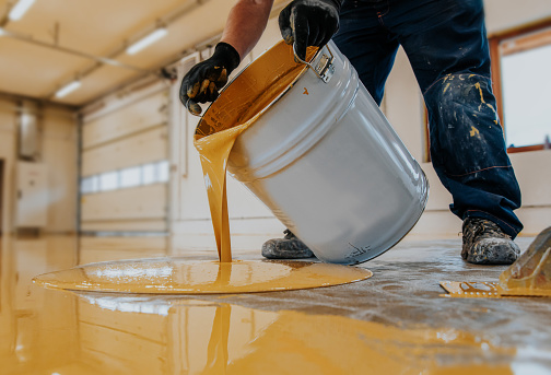 Trabajador aplicando un cubo de resina epoxi amarillo en el suelo para la capa final. photo
