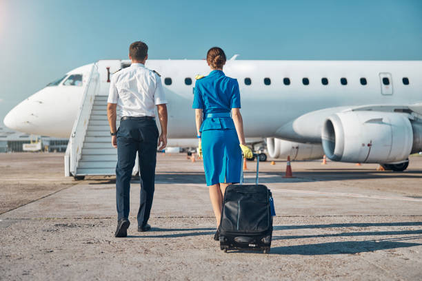 Pilot and stewardess boarding before working trip Man and woman in aviation uniform are walking to plane stairway with luggage before departure crew stock pictures, royalty-free photos & images