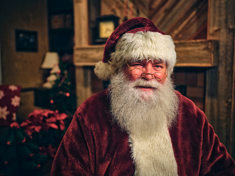 Santa Claus in eyeglasses is looking at camera and smiling, on gray background