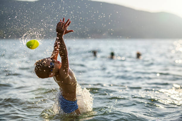 Brother and sister enjoying sunny summer day on beach.\nKids are playing catch with small ball in the sea. Little boy is jumping to the ball trying to catch it.\nNikon D850