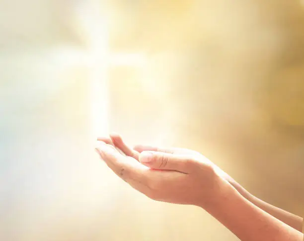 Prayer open empty hands with palm up over blurred cross with golden light background