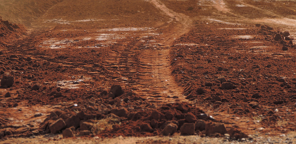 Large stock image of a red sandy dusty road with tire tracks on it looking like the planet Mars. Selective focus on the center of the image and blurred edges