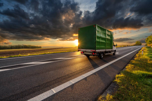 furgoneta de reparto conduciendo por la carretera de asfalto en el paisaje rural en los rayos de la puesta de sol con nube oscura - small truck fotografías e imágenes de stock