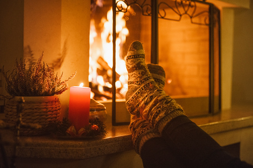 Beautiful photo of a unrecognizable man that is warming his feet on the fireplace wearing Christmas  socks