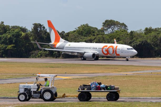 Tractor for the baggage transport and a airplane Santarem/Para/Brazil - Sep 29, 2020: Tractor for the baggage transport service at Santarem Airport (SBSN) and a GOL Airlines plane in the background. stm photos stock pictures, royalty-free photos & images